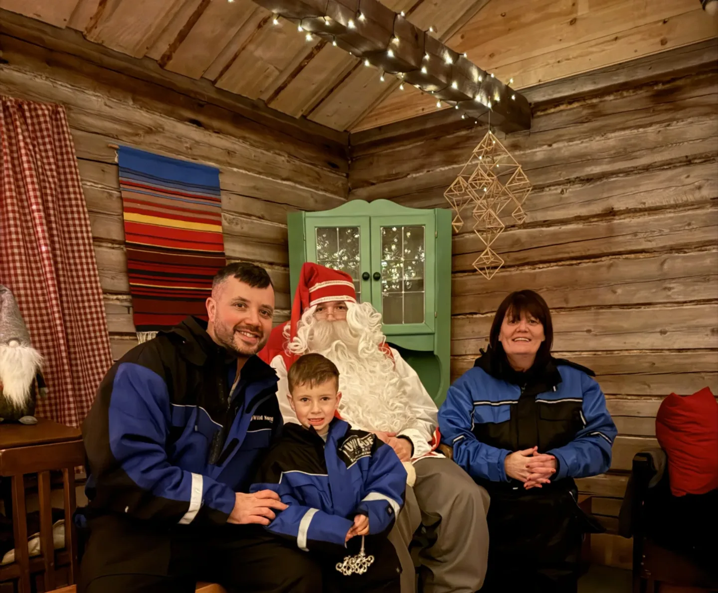 A family sitting with Santa Claus in a log cabin decorated with fairy lights